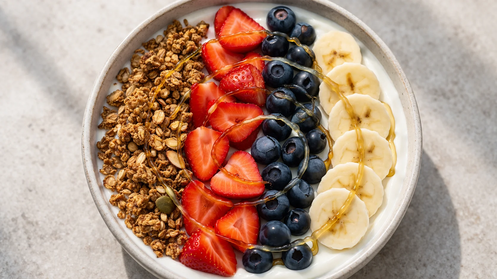 Gros plan sur les couches du bowl : fromage blanc cremeux, granola doré et fruits frais colorés