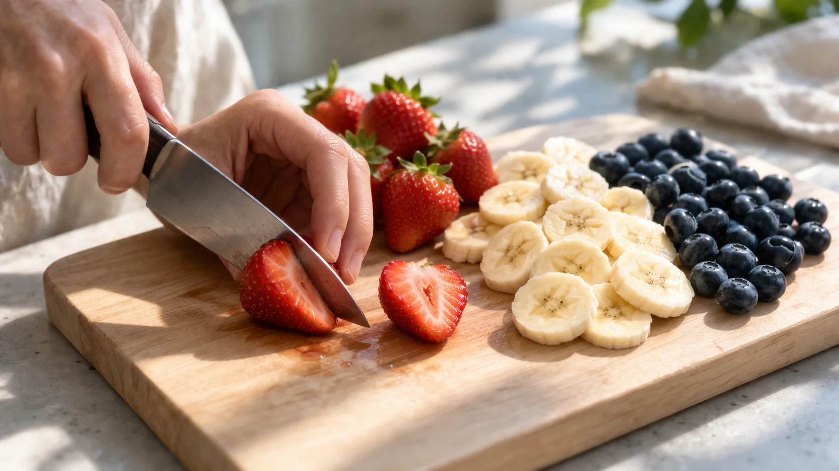 Fraises équeutées et coupées, rondelles de banane et myrtilles fraîches préparées sur une planche à découper en bois clair