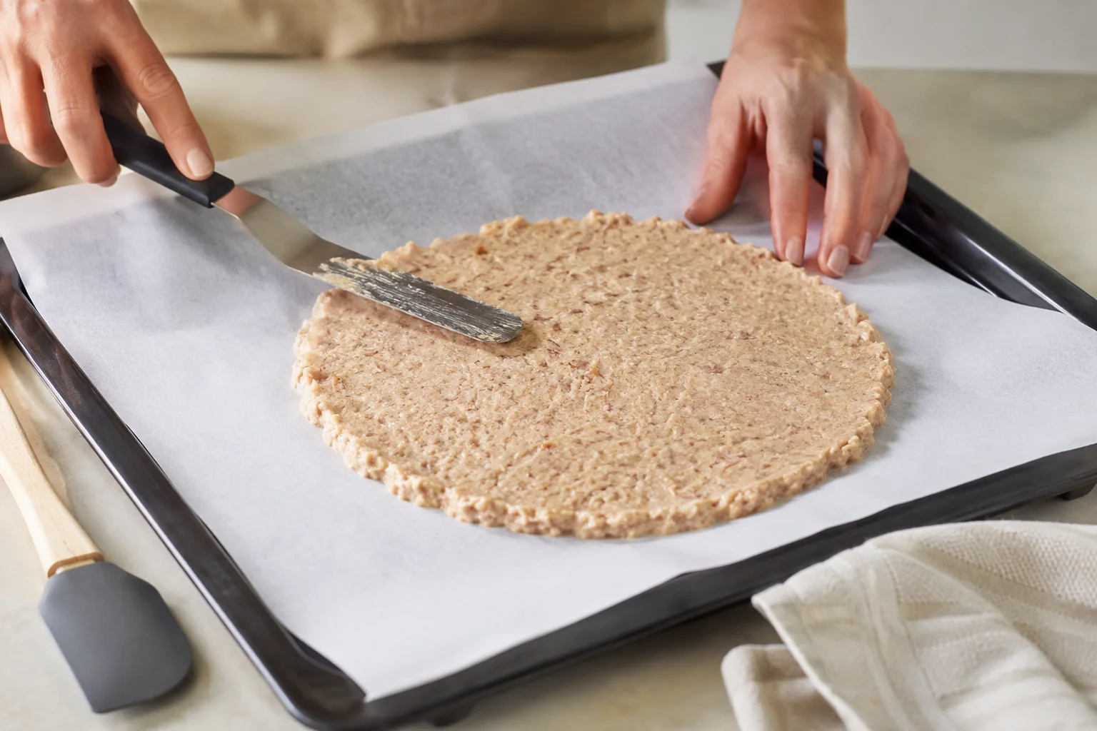 Mains qui étalent une pâte au thon en disque rond sur une feuille de papier sulfurisé blanc, spatule à côté