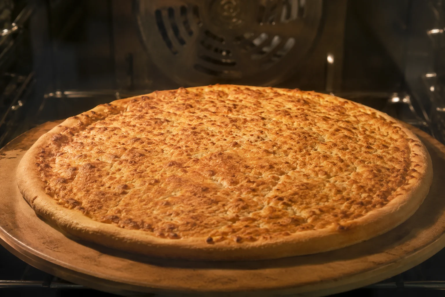 Base de pizza au thon en train de dorer dans un four chaud, surface brun-doré uniforme et légères craquelures visibles